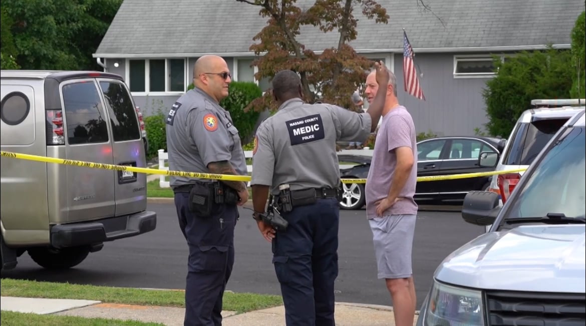 เข้าหน้าที่ตำรวจกำลังยืนคุยกับช่วบ้านท่านหนึ่งที่กำลังบยืนเท้าเอวเล่าเหตการณ์