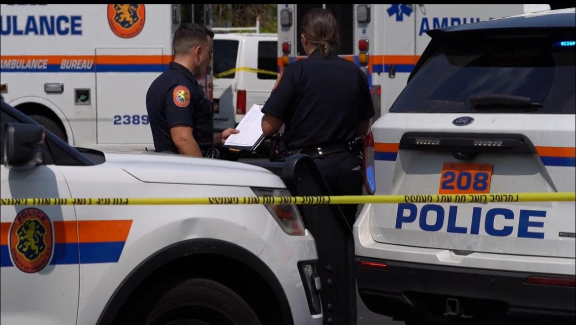 เจ้าหน้าที่ตำรวจยืนอยู่ท้ายรถฉุกเฉิน ในที่เกิิดเหตุฆาตกรรม