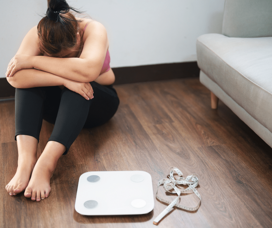 คนกำลังเครียด นั่งอยู่ที่พื้น โดยรอบมีเครื่องชั่งน้ำหนัก