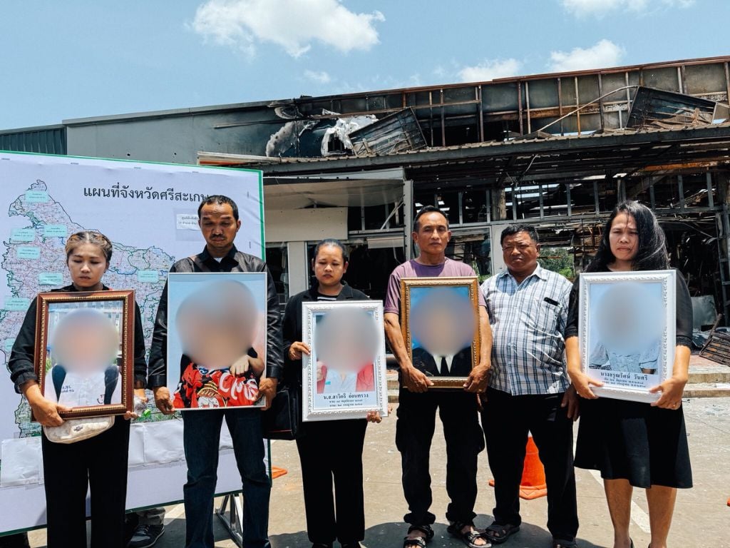 ญาติผู้เสียชีวิตยืนถือกรอบรูปถ่ายท่ามกลางซากปรักหักพังของปั๊มน้ำมัน ปตท.