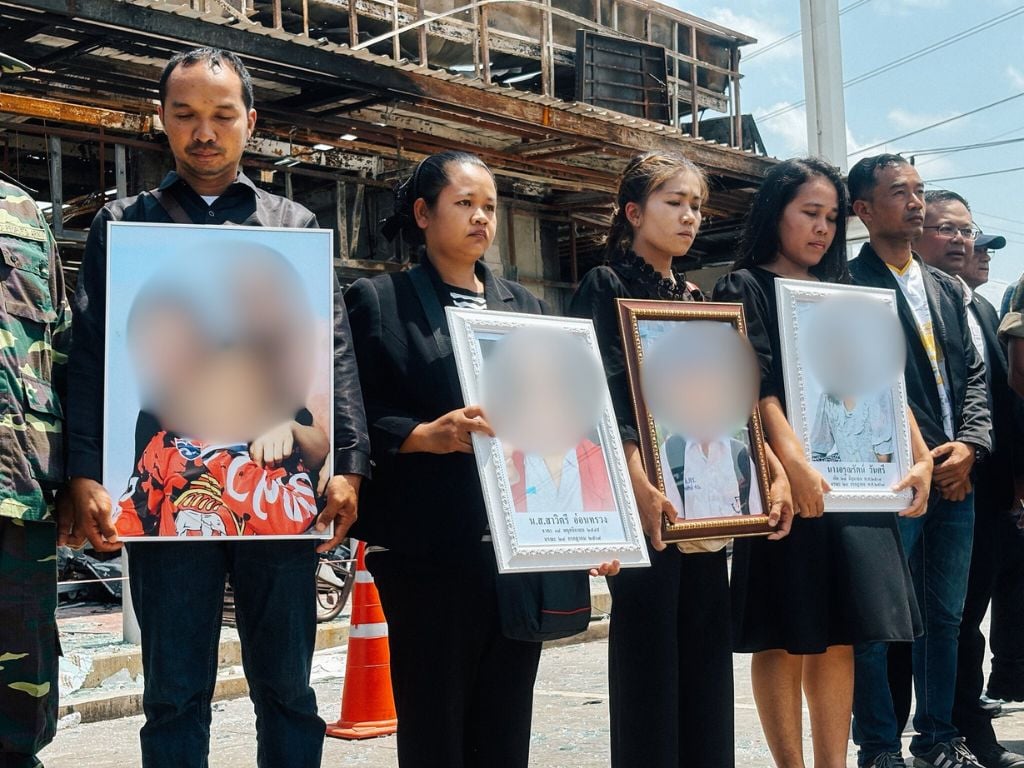 ญาติผู้เสียชีวิตยืนถือกรอบรูปถ่ายท่ามกลางซากปรักหักพังของปั๊มน้ำมัน ปตท.