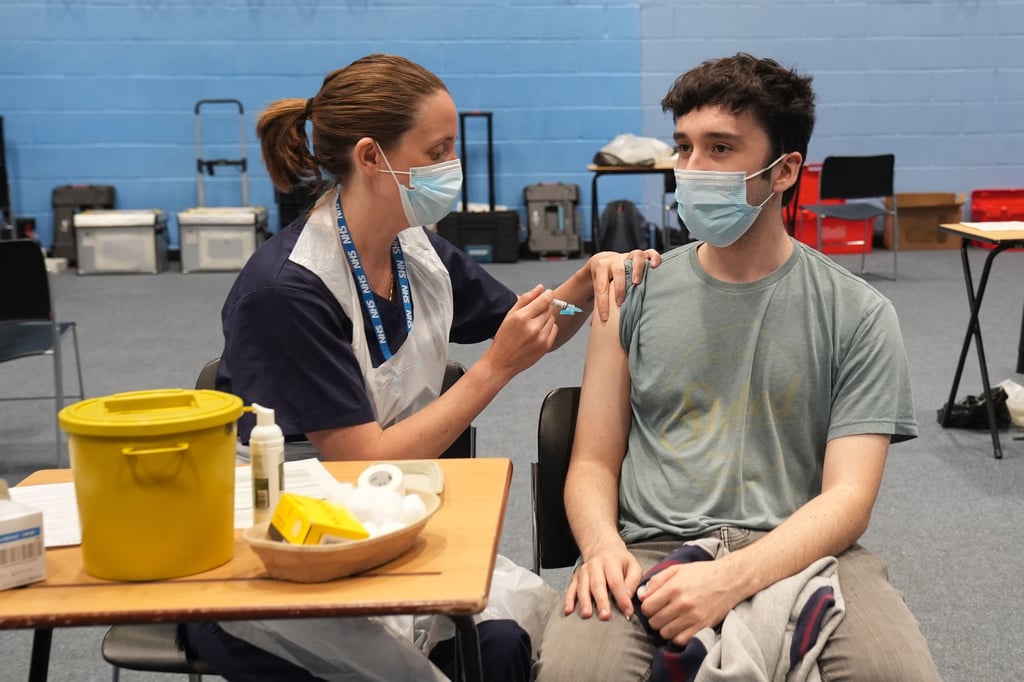 22-year-old postgraduate law student Oliver Contreras, right, receives an injection in the sports hall at the University of Kent campus in Canterbury, England, Wednesday, March 18, 2026, where the rollout of a meningitis B vaccine to about 5,000 students has begun.