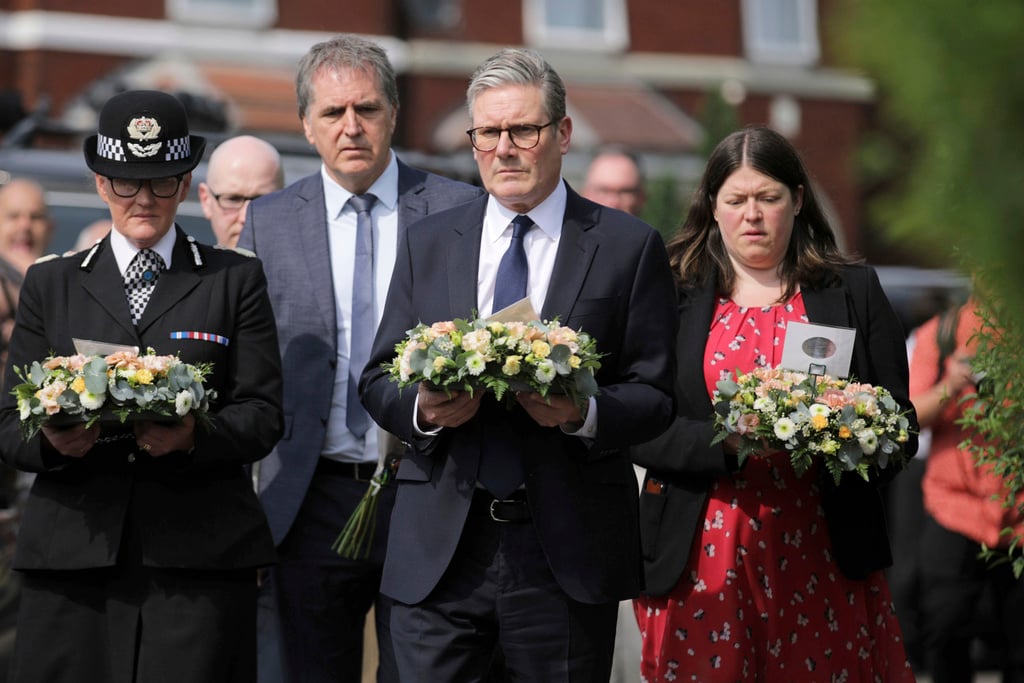 British Prime Minister Keir Starmer, center, carries a floral tribute near the scene in Hart Street, where three children died and eight were injured in a knife attack during a Taylor Swift event at a dance school on Monday, in Southport, England, Tuesday, July 30, 2024. 