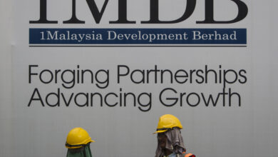 Construction workers chat in front of a billboard for state investment fund 1 Malaysia Development Berhad (1MDB) at the fund's flagship Tun Razak Exchange development in Kuala Lumpur, Malaysia, on May 14, 2015. (AP Photo/Joshua Paul, File).