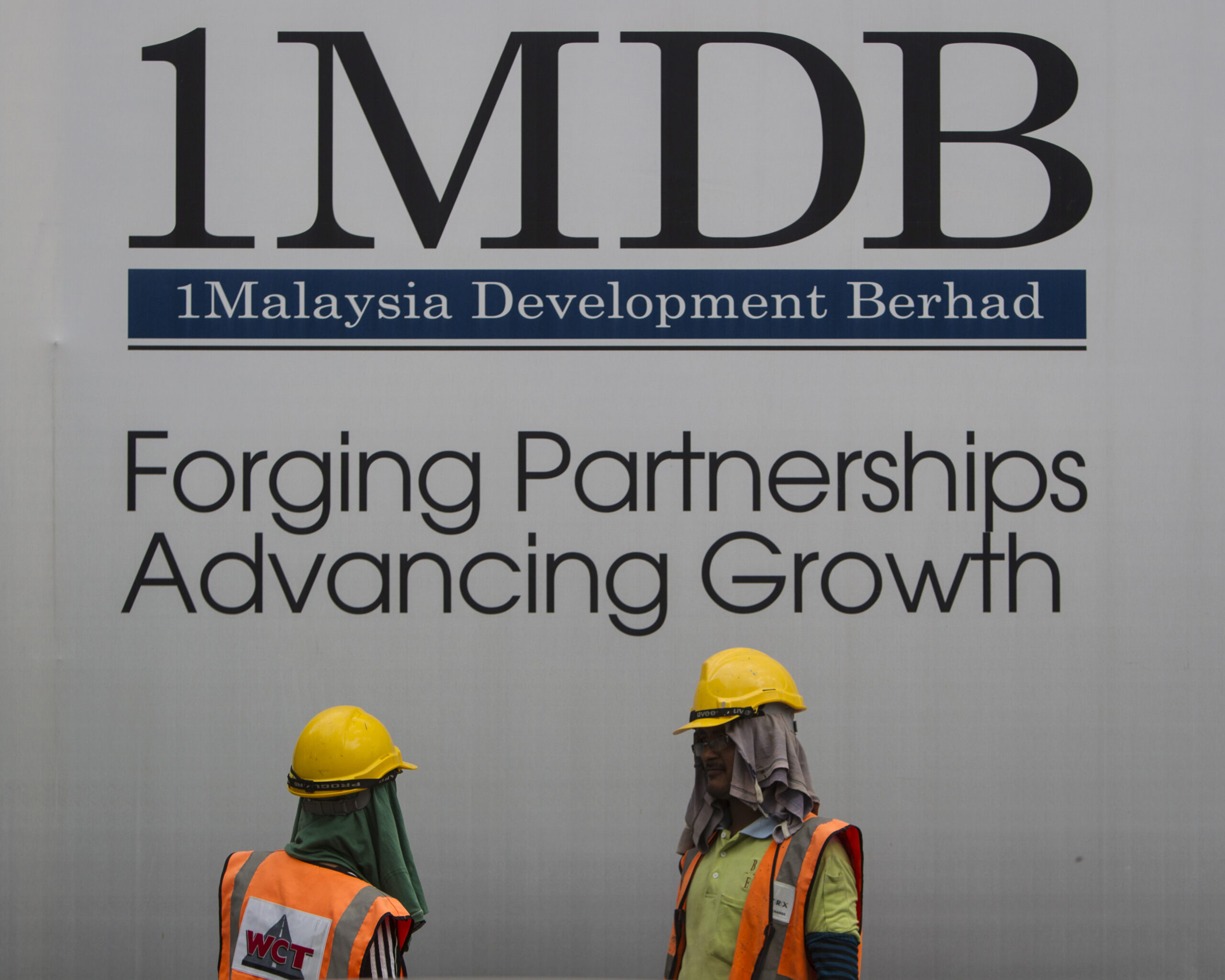 Construction workers chat in front of a billboard for state investment fund 1 Malaysia Development Berhad (1MDB) at the fund's flagship Tun Razak Exchange development in Kuala Lumpur, Malaysia, on May 14, 2015. (AP Photo/Joshua Paul, File).