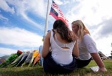 Two students view a memorial as the flags fly half-staff after a shooting Wednesday at Apalachee High School, Thursday, Sept. 5, 2024, in Winder, Ga. (AP Photo/Mike Stewart).