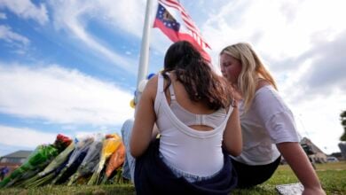 Two students view a memorial as the flags fly half-staff after a shooting Wednesday at Apalachee High School, Thursday, Sept. 5, 2024, in Winder, Ga. (AP Photo/Mike Stewart).