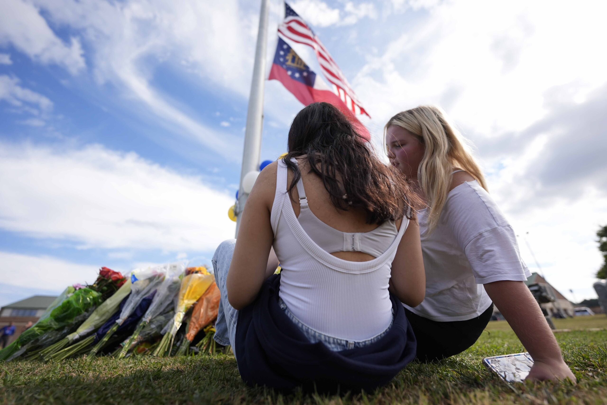 Two students view a memorial as the flags fly half-staff after a shooting Wednesday at Apalachee High School, Thursday, Sept. 5, 2024, in Winder, Ga. (AP Photo/Mike Stewart).