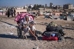 An elderly Palestinian man in a wheelchair waits with his belongings to flee the Khan Younis area of the Gaza Strip, Aug. 8, 2024, after Israeli military evacuation orders that said its forces would soon operate in the area. (AP Photo/Abdel Kareem Hana).