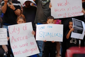 Residents hold up placards during a rally staged by the East Colfax Community Collective to address chronic problems in the apartment buildings occupied by people displaced from their home countries in central and South America Tuesday, Sept. 3, 2024, in Aurora, Colo. (AP Photo/David Zalubowski).