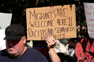 A protester holds up a placard during a rally staged by the East Colfax Community Collective to address chronic problems in the apartment buildings occupied by people displaced from their home countries in central and South America Tuesday, Sept. 3, 2024, in Aurora, Colo. (AP Photo/David Zalubowski).