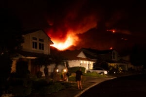 A man watches flames from the Airport Fire as it envelops a hill behind homes Monday, Sept. 9, 2024, in Trabuco Canyon, Calif. (AP Photo/Gregory Bull).