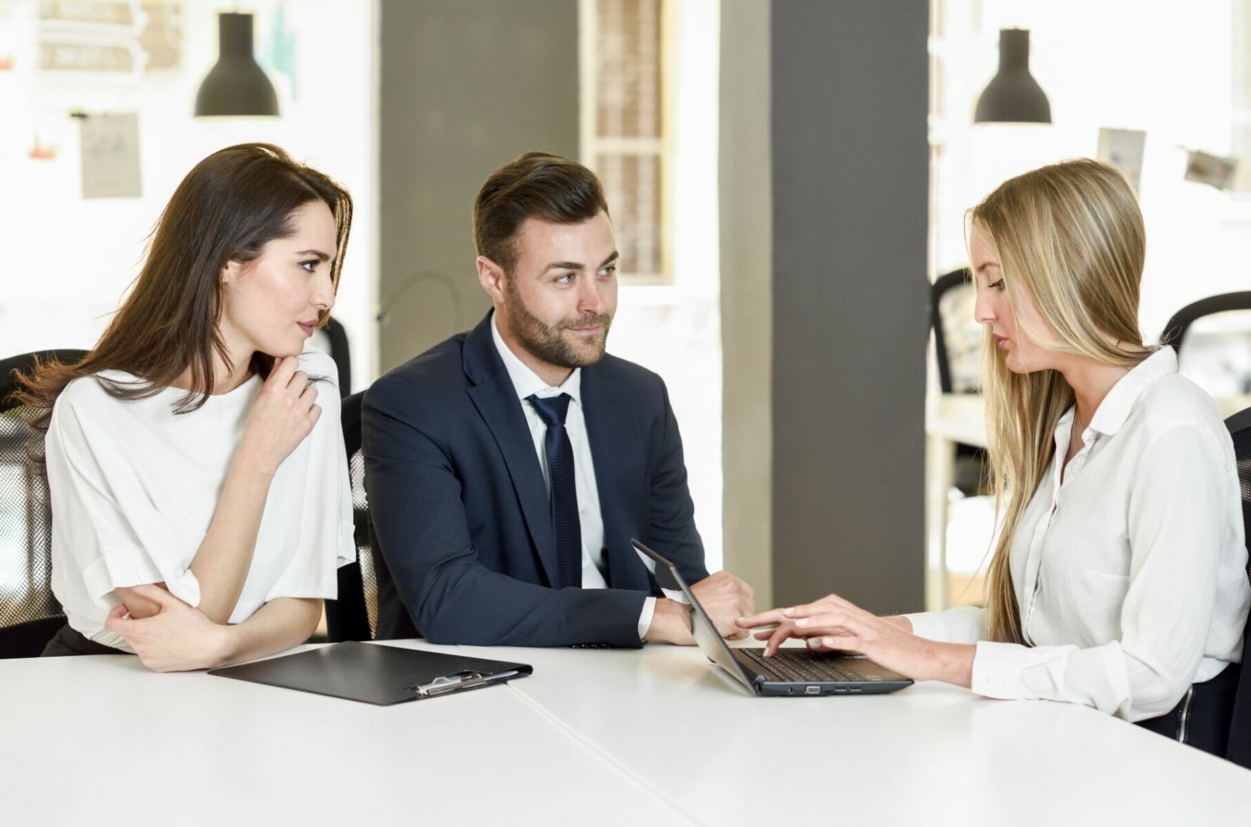 Blonde businesswoman explaining with laptop to smiling young couple