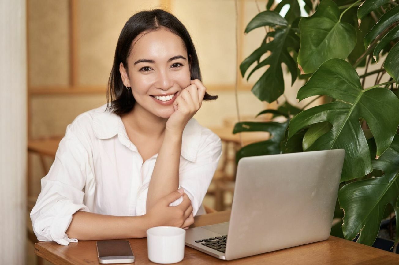 Smiling female with laptop in cafe after signing up for a car subscription service by Carzuno