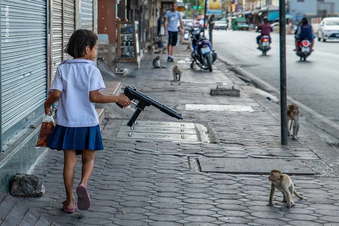 Thai girl points air gun at monkey in Lop Buri