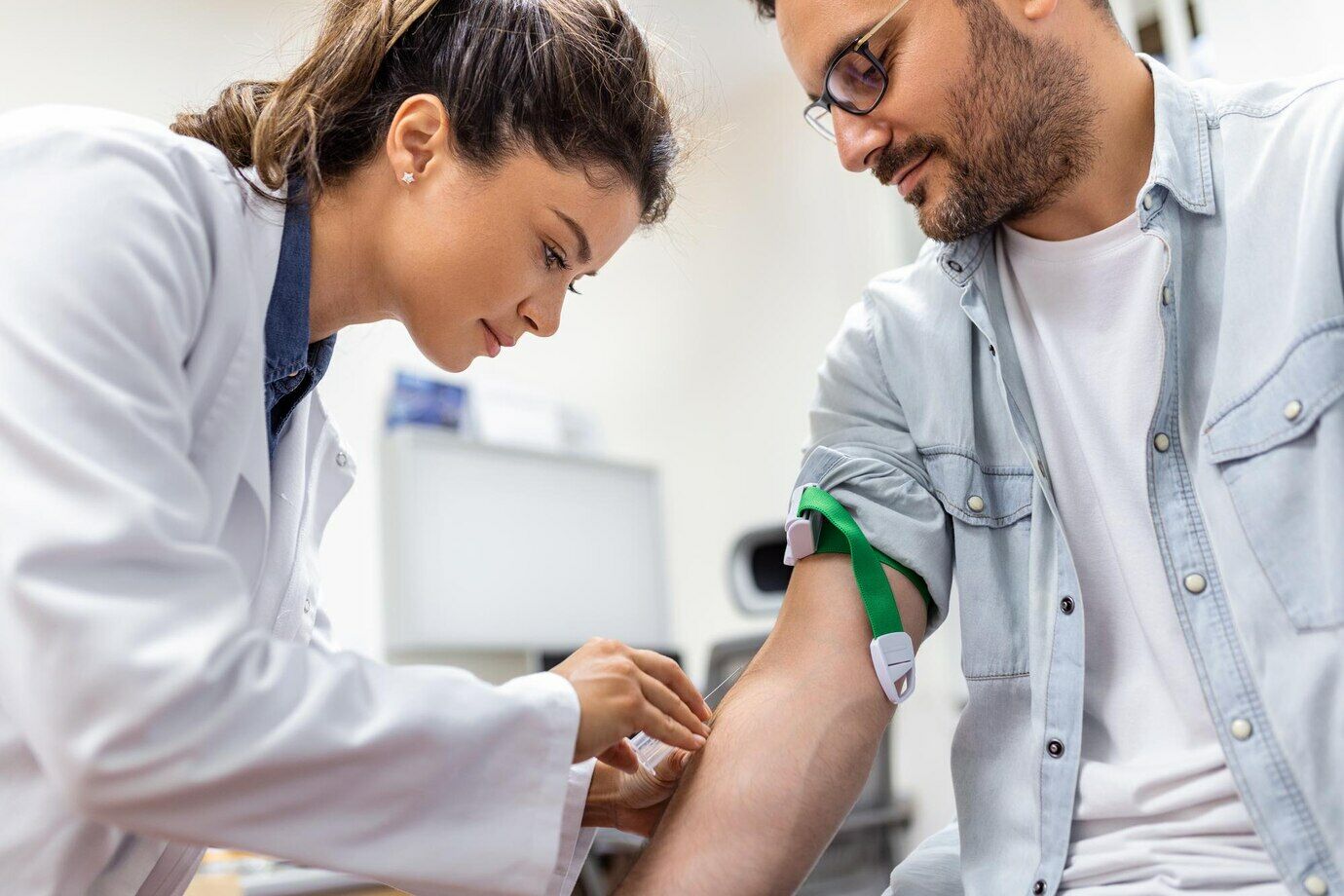 Friendly hospital phlebotomist collecting blood sample from patient in lab Preparation for blood test by female doctor medical uniform on the table in white bright room