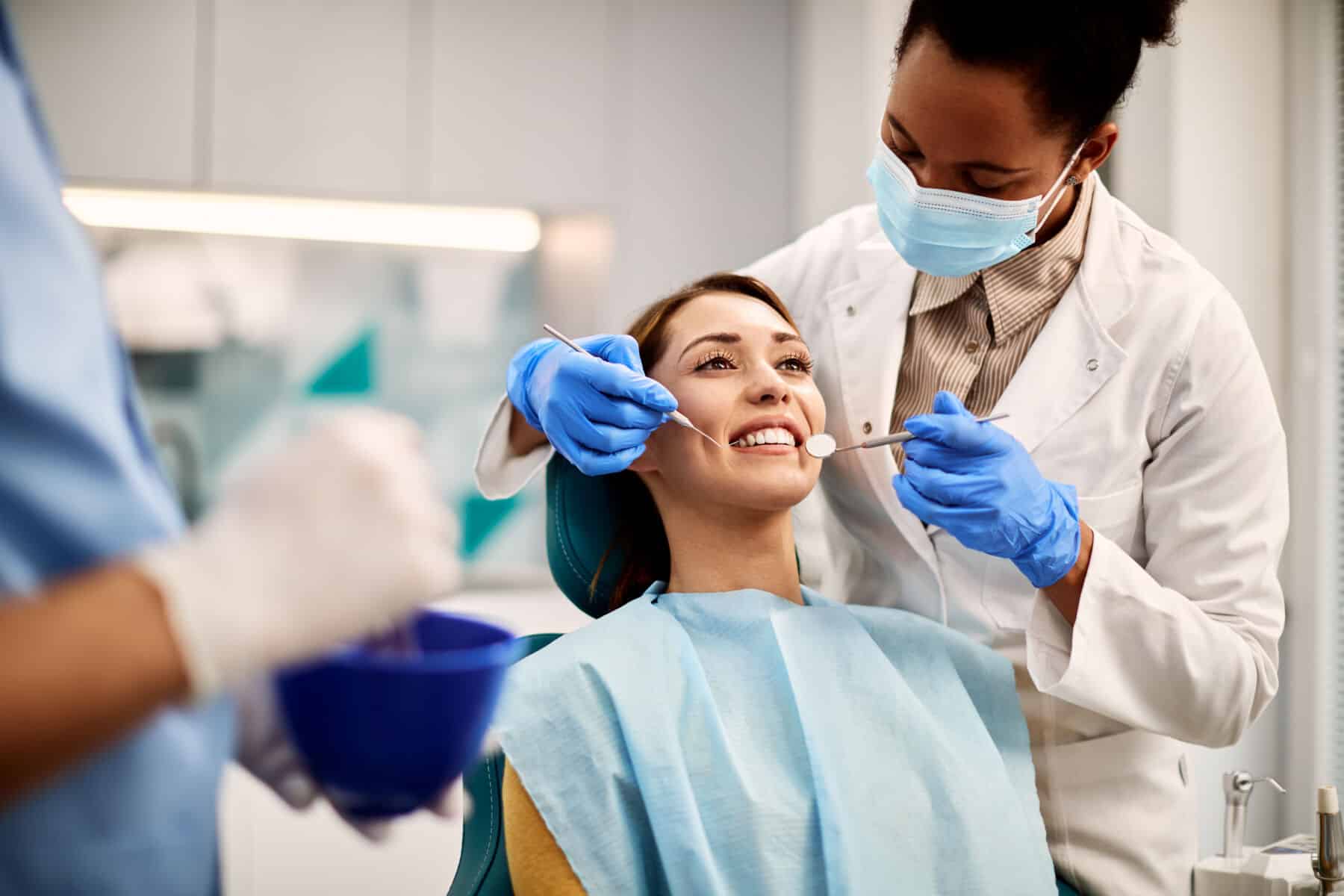 Smiling woman getting her teeth checked by African American dentist at dental clinic in Thailand