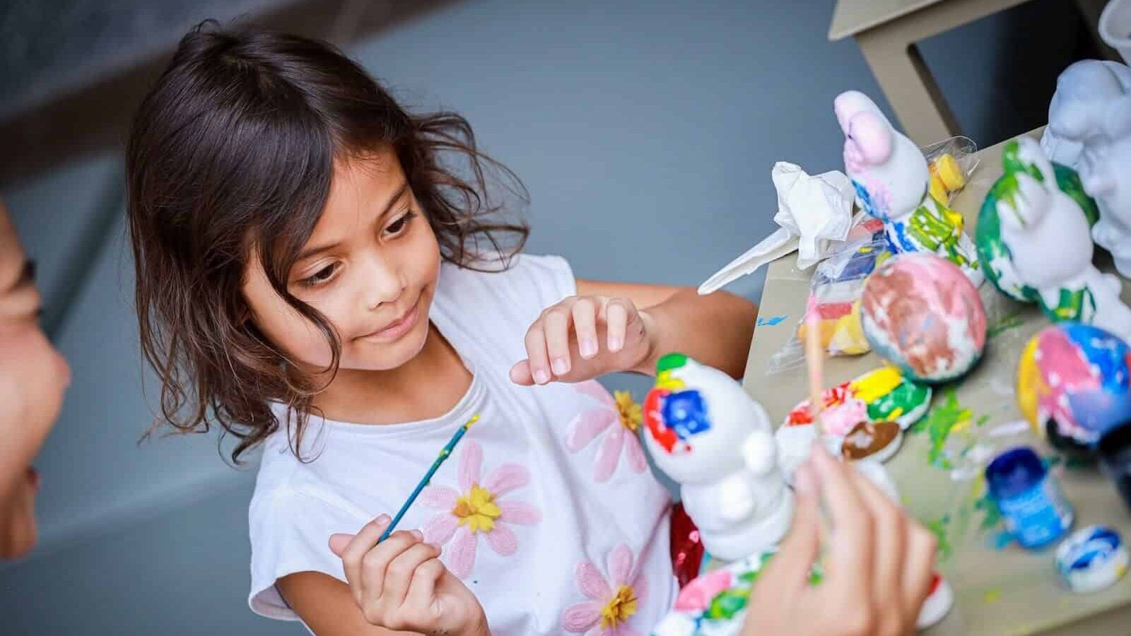 Young girl painting ceramic figurines during a kids' activity in a beach club in Thailand