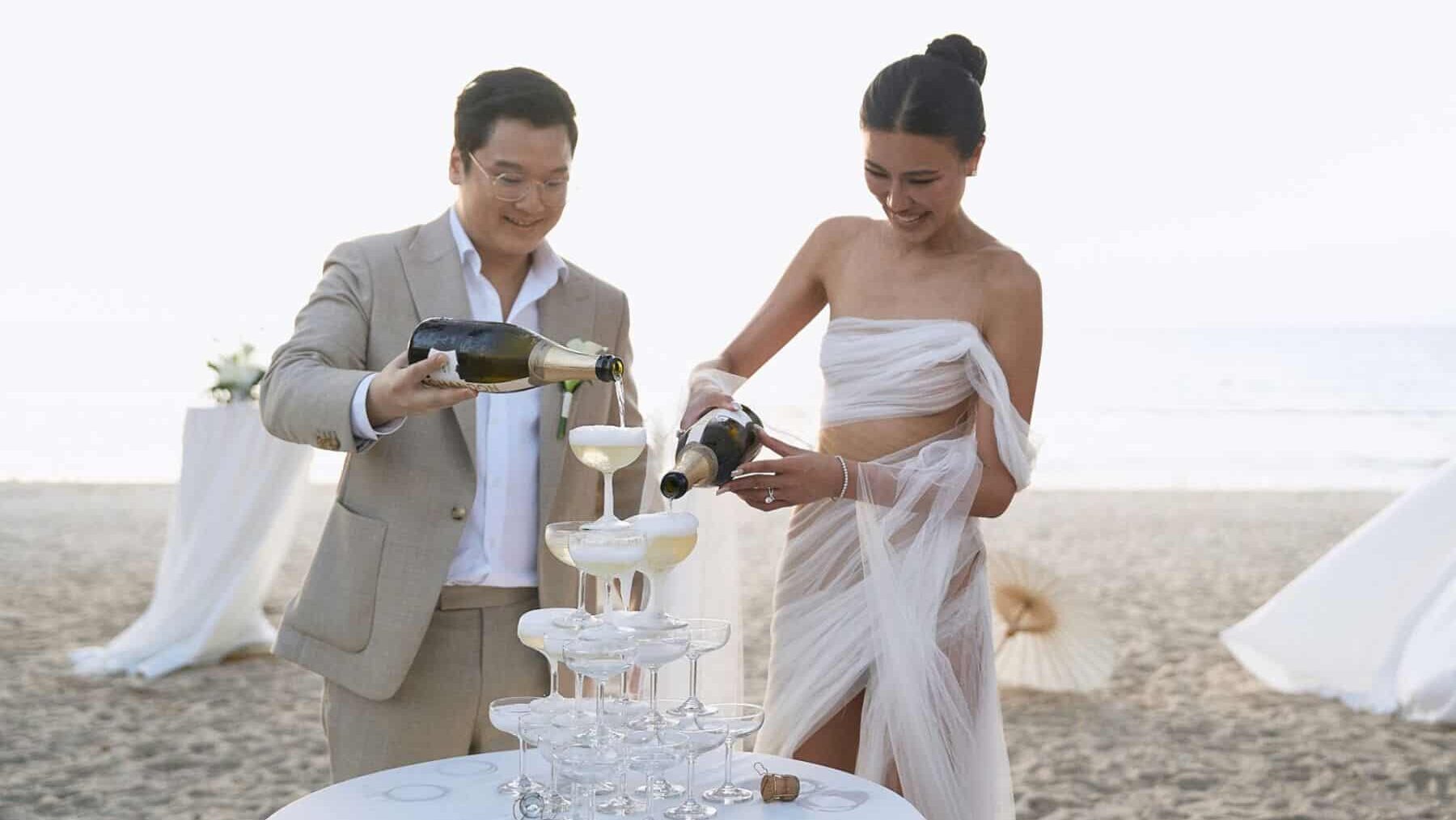 Bride and groom pouring champage at a beach wedding ceremoni at Nora Beach Club, Phuket, Thailand