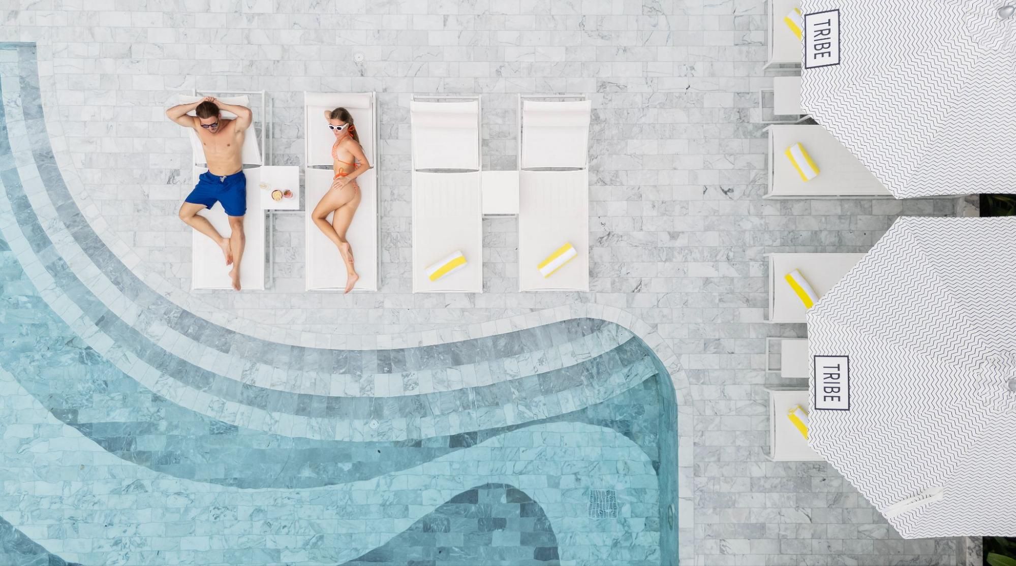 A couple relaxing on white sun loungers beside the marble-tiled pool at a hotel in Phuket