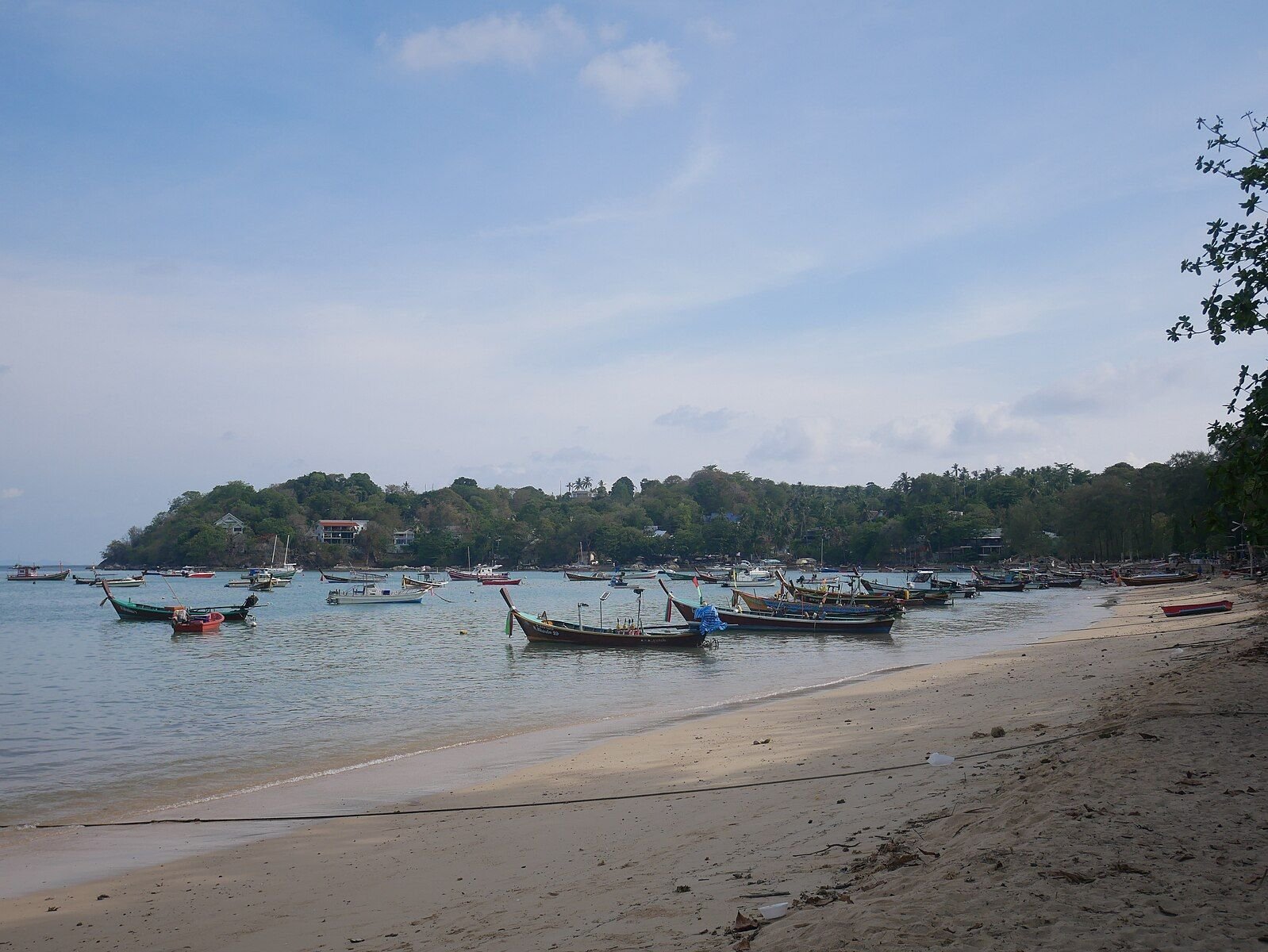Traditional longtail boats anchored along Rawai Beach in Phuket on a sunny day.