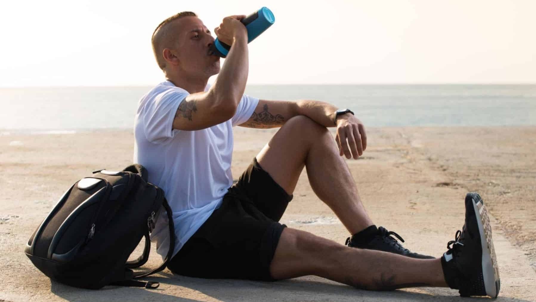 A man drinking water while sitting down by the water