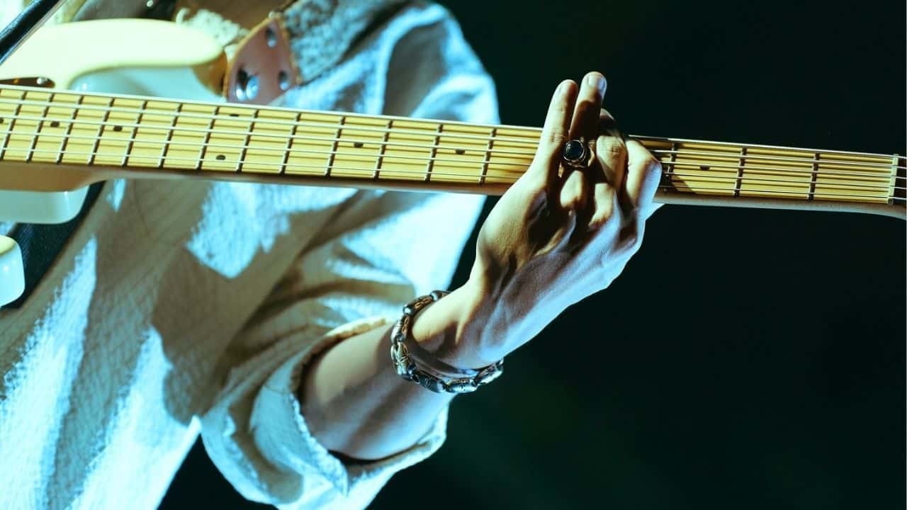 A close-up of LINION gripping his bass guitar during a live performance.