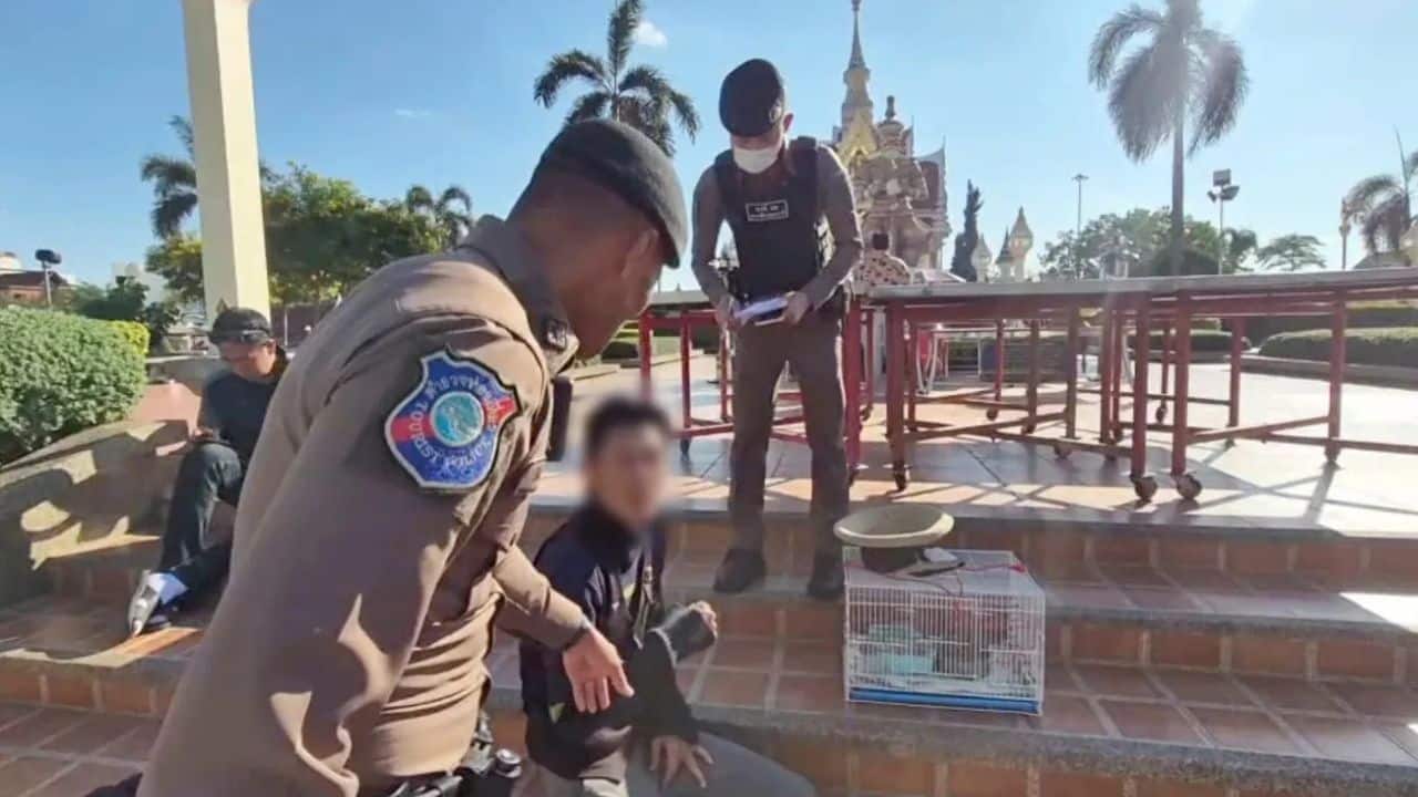 Police officers speak with Japanese man Yamaguchi at Udon Thani shrine, with a birdcage nearby.