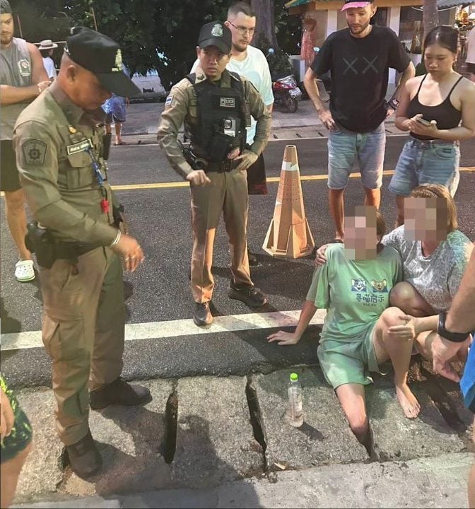 Sakhu Police and bystanders assist a Russian tourist whose right leg is trapped in a drainage opening at Naithon Beach, Phuket.